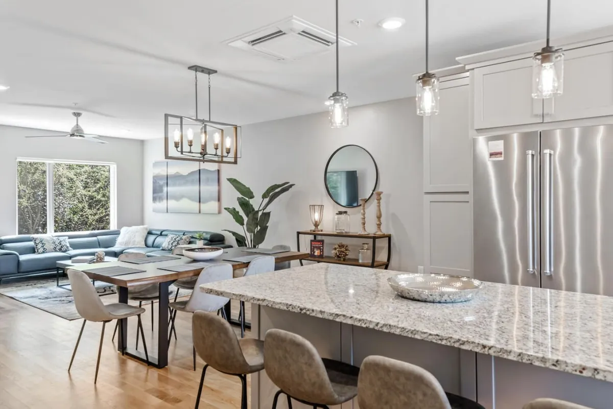 A bright, open-plan space unites a modern kitchen with a sleek island, a spacious dining table, and a comfortable seating area. The room feels inviting, with thoughtful lighting and plenty of space to gather for meals or socialize. Subtle details, such as elegant finishes and contemporary décor, add to the sense of sophistication and warmth.