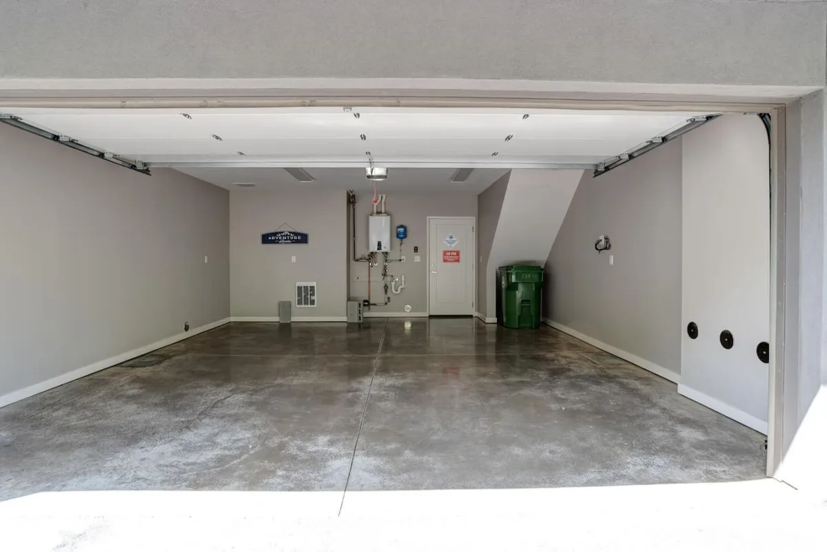A garage interior focusing on the garage door as it opens, with a water heater and green trash bin. The scene evokes readiness for arrival and departure, supporting a narrative of ease and practicality.