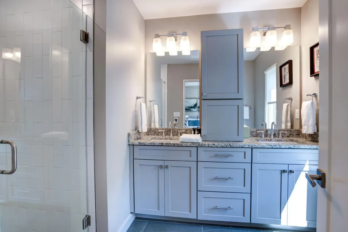 A contemporary bathroom featuring double sinks set in a granite countertop, a sleek glass shower enclosure, and ample light. The space feels serene and spa-like, perfect for moments of self-care and relaxation.