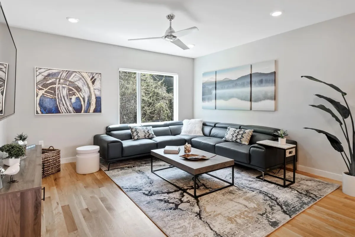 A calm and modern living space featuring a sofa, coffee table, contemporary artwork, and a window offering an uplifting view. The setting suggests a space for unwinding, reading, or enjoying conversation, with a tranquil ambiance.