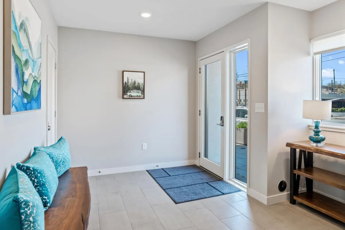 A welcoming entryway featuring a turquoise bench with cushions, a wooden table, artwork, and the front door. Bright, inviting, and designed for first impressions.